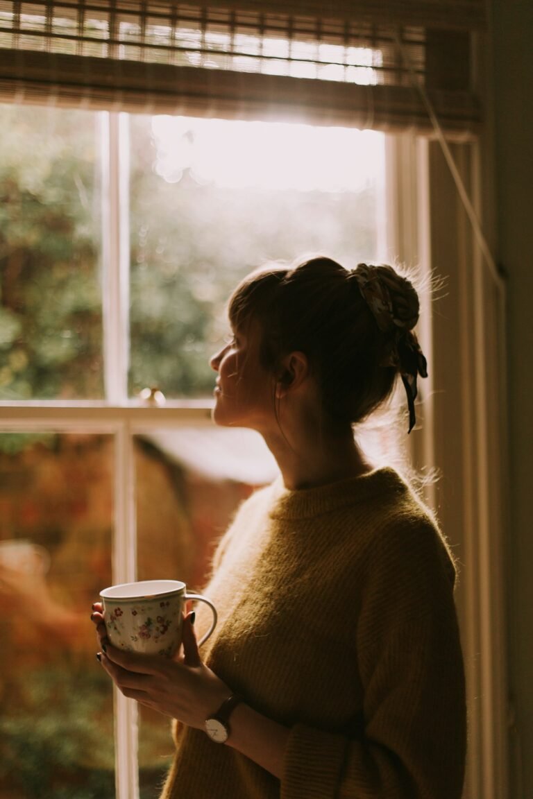 Woman holding a cup of tea by a sunlit window, reflecting on modern womanhood