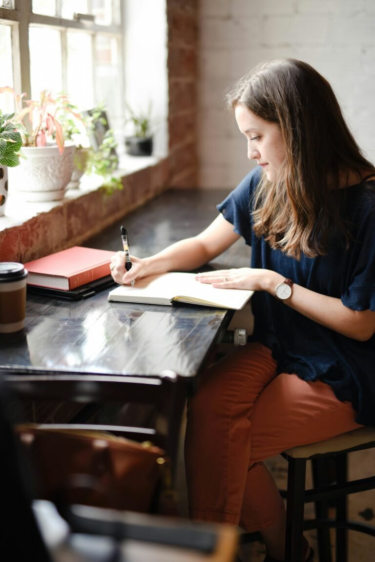 Woman writing in a journal by the window as part of her personal growth routine