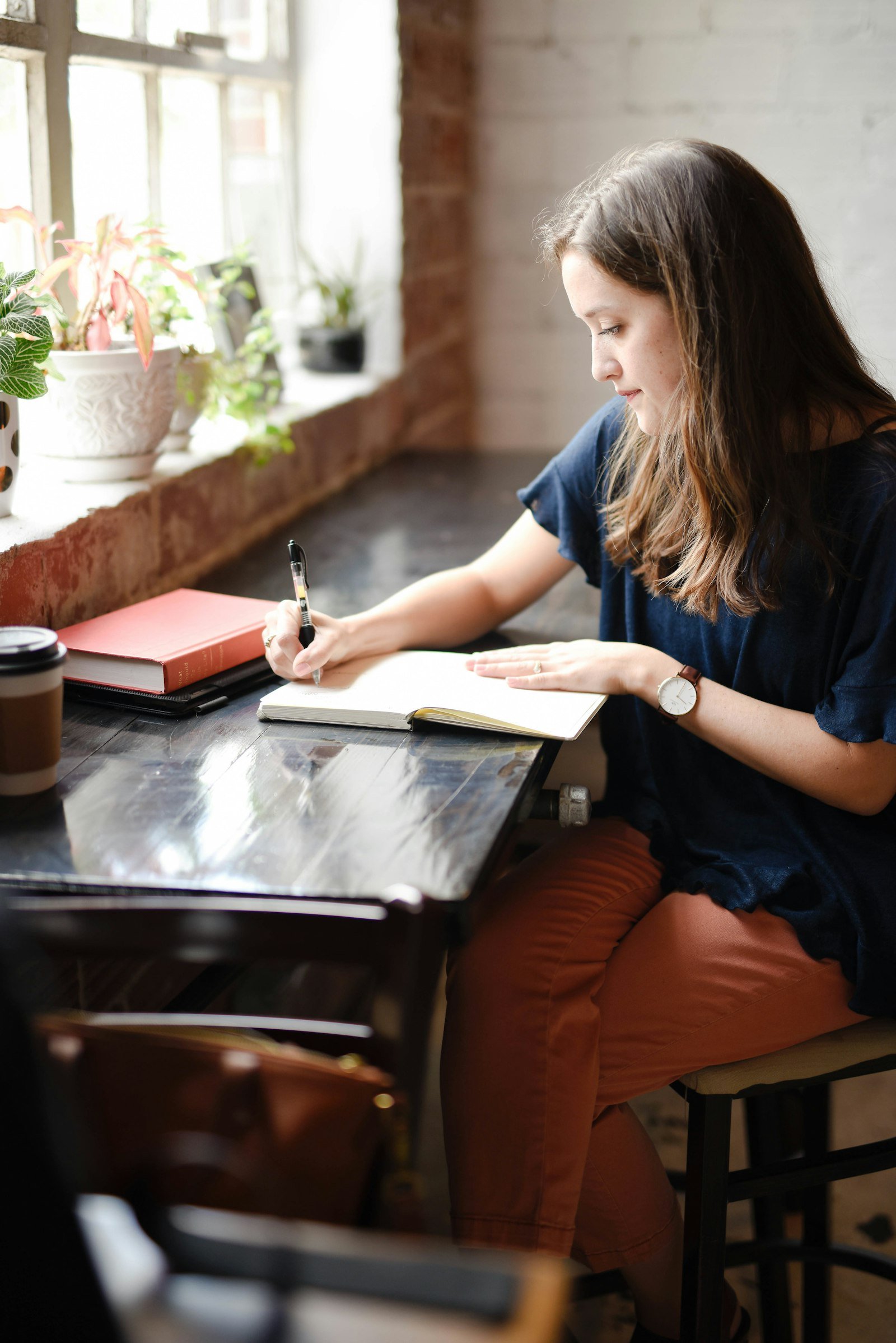Woman writing in a journal by the window as part of her personal growth routine