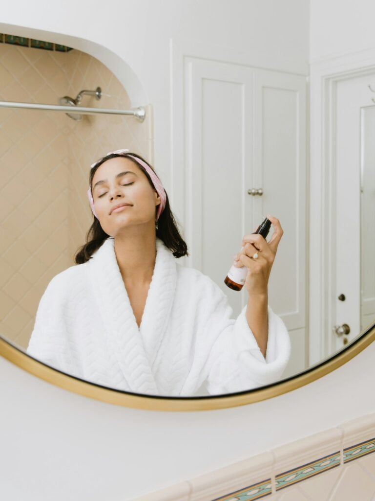 Woman in a white robe spraying facial mist during her skincare routine